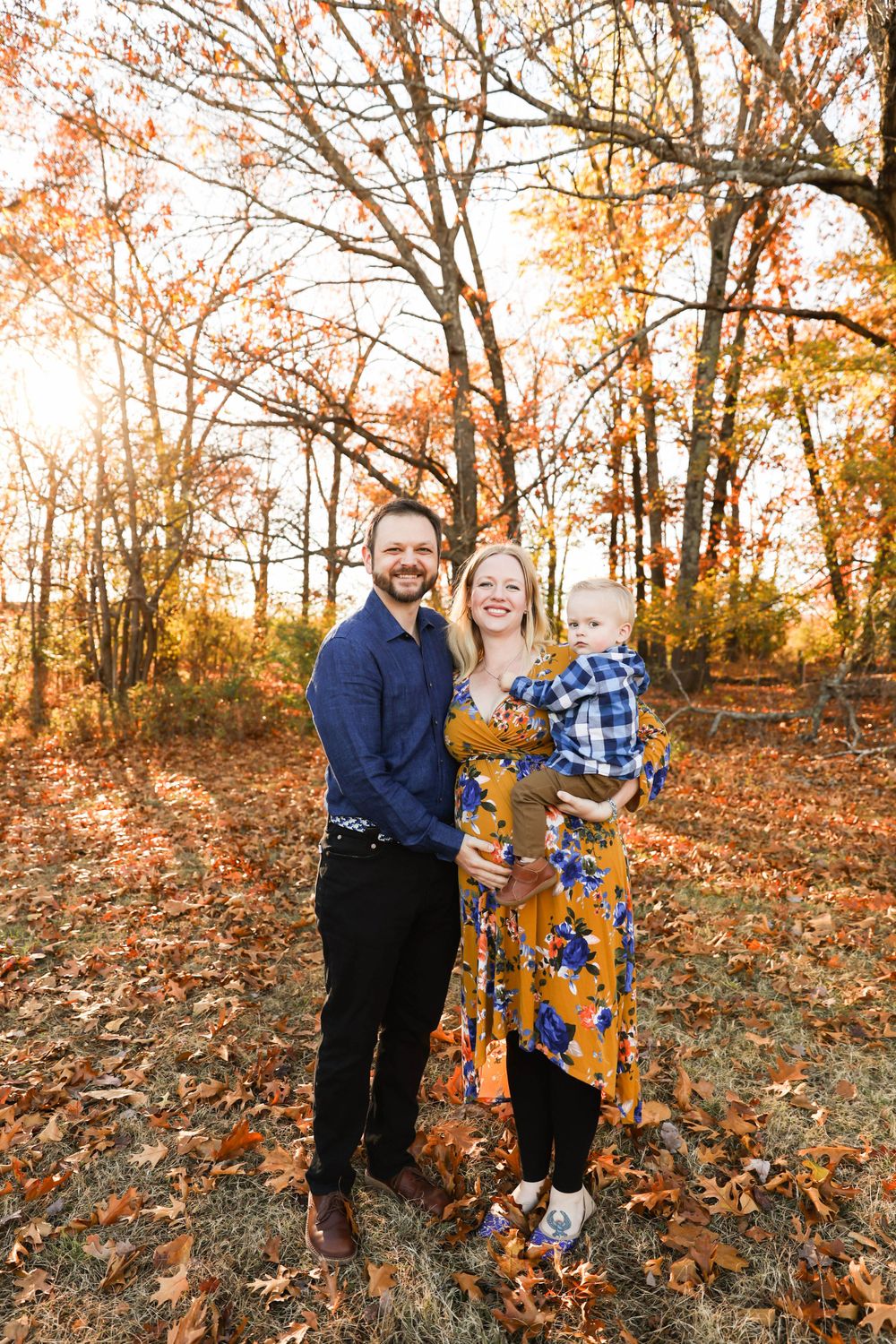 A family poses together in a forest with vibrant fall foliage and warm sunlight filtering through trees.