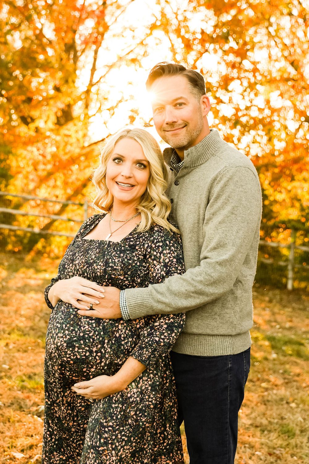 Expecting couple poses together against vibrant autumn foliage backdrop.
