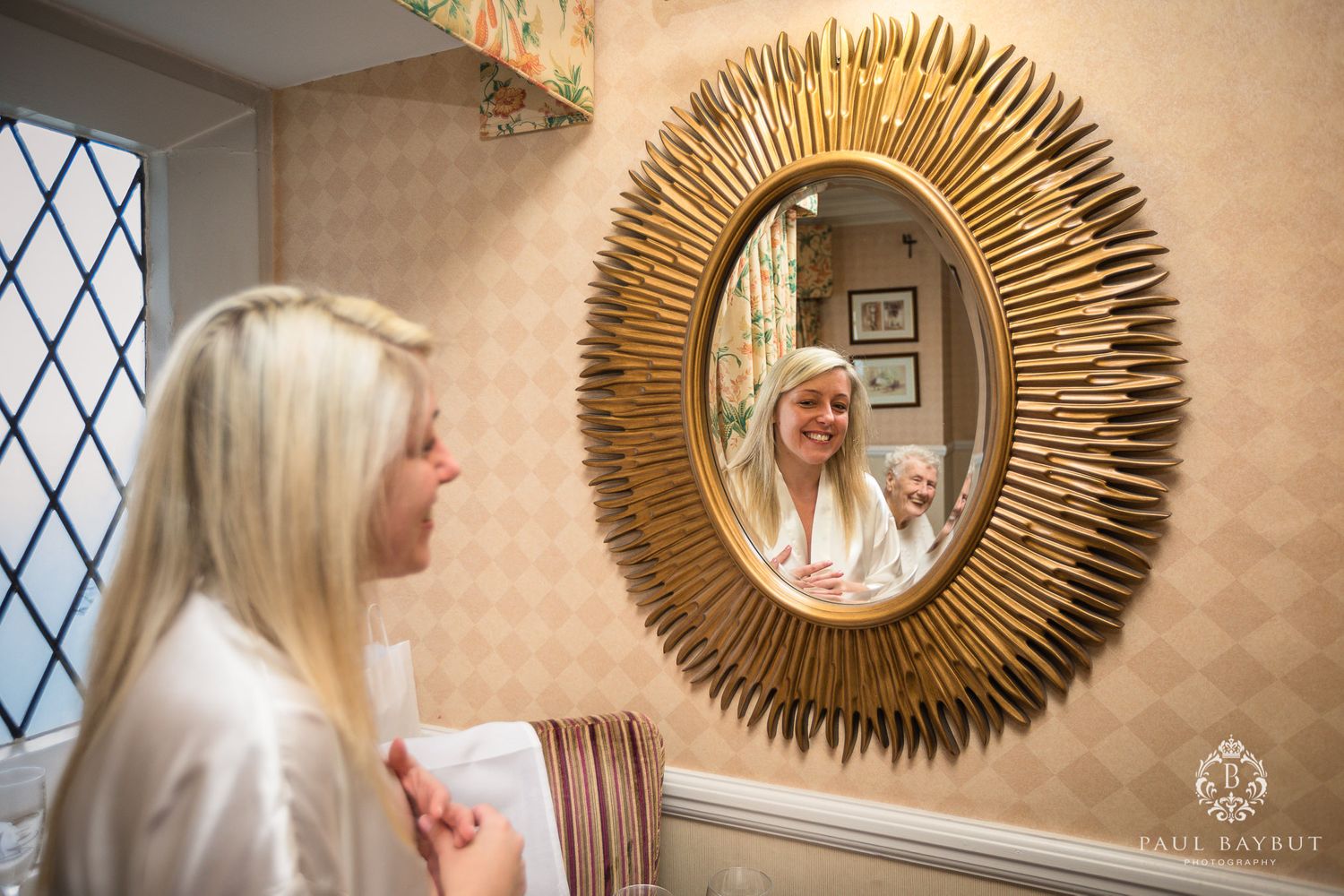 Gold sunburst mirror reflects a view in an elegant room with diamond-paned window.