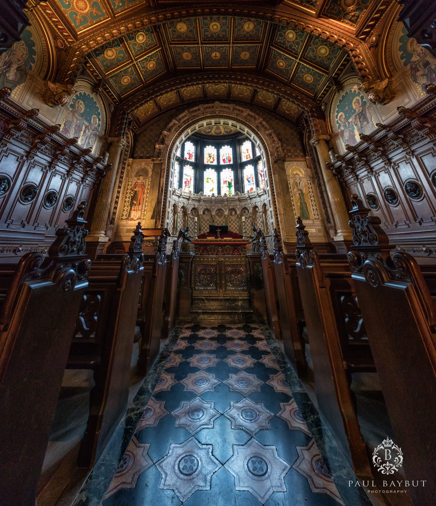 Ornate chapel interior with vaulted ceiling, stained glass windows and checkered floor.