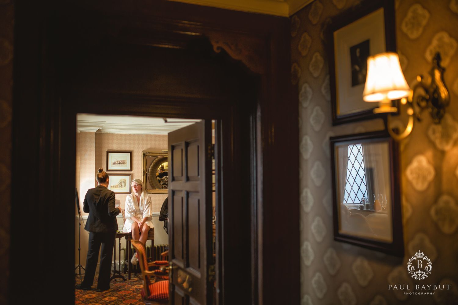Silhouetted figures seen through doorway in dimly lit vintage interior with wallpaper.