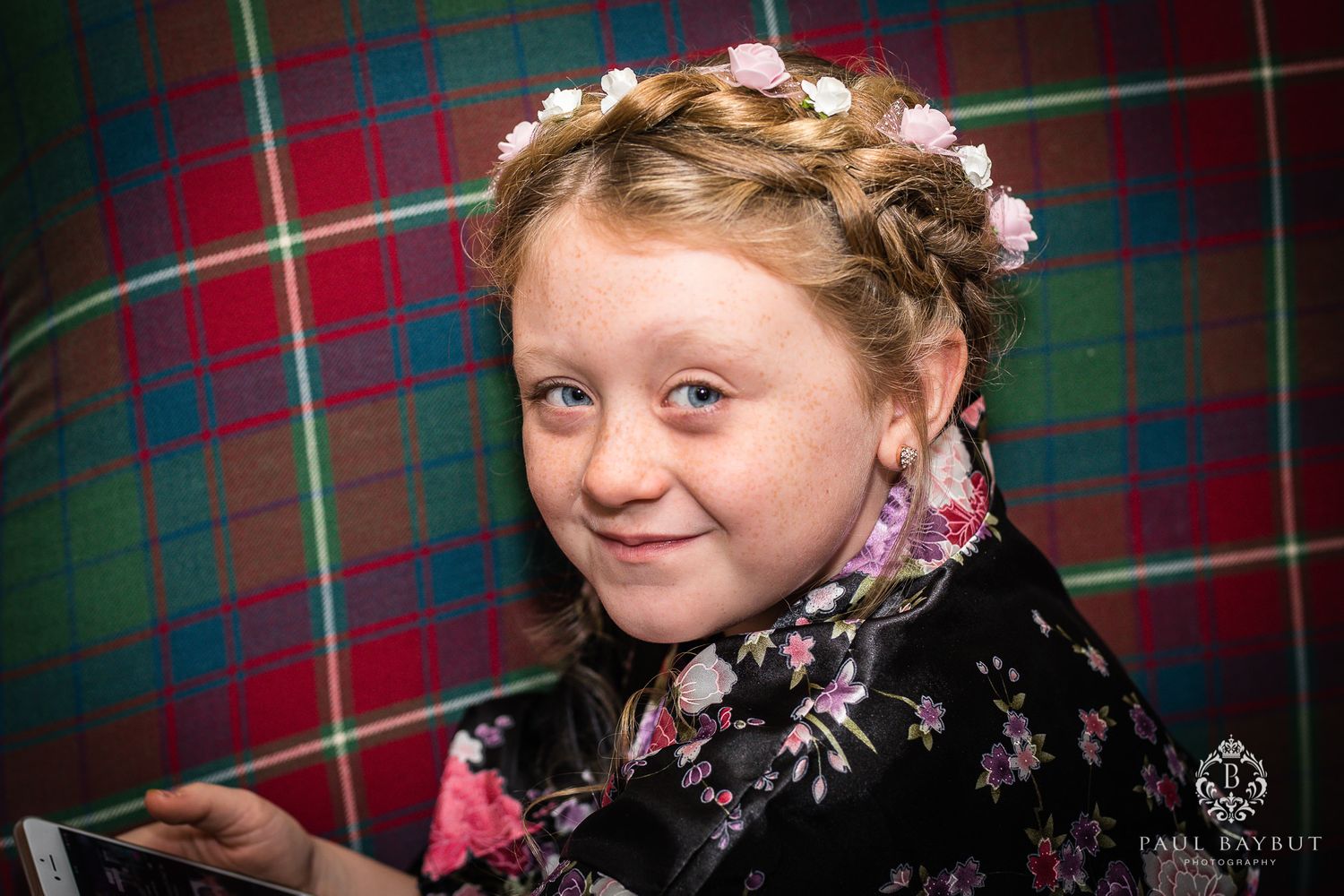 A floral-patterned outfit against a red and green tartan background with flowers in hair.