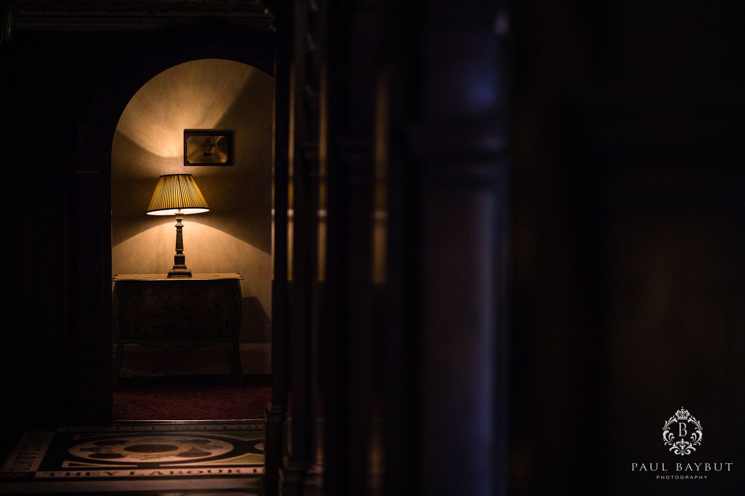 Moody corridor with lamp illuminating an arched alcove in dim lighting.