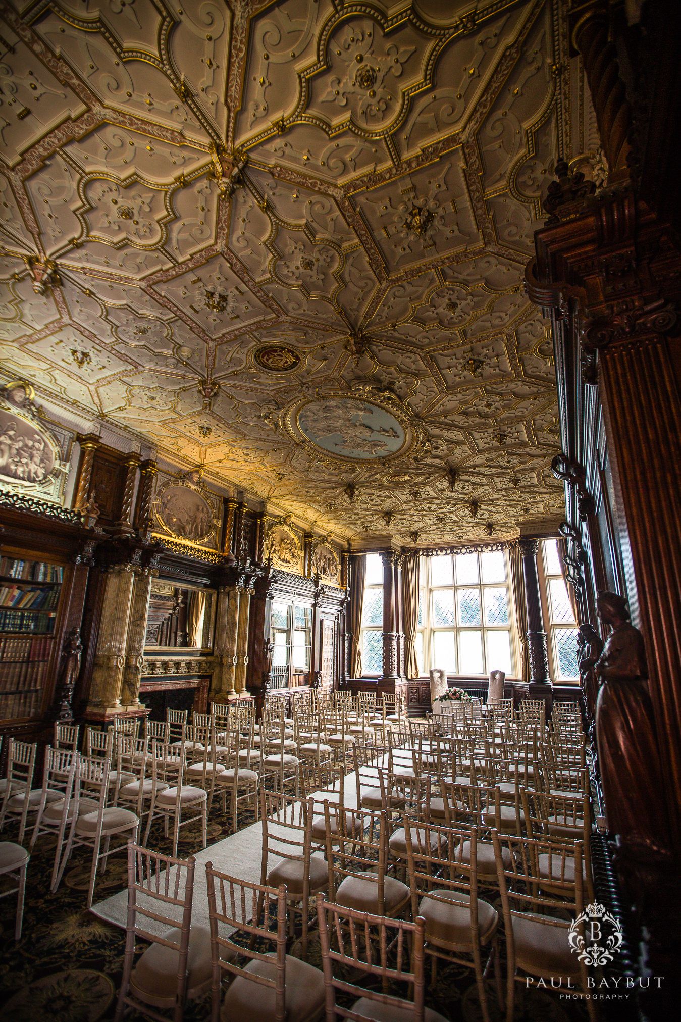 Grand room with intricate plasterwork ceiling and white chiavari chairs arranged in rows for an event.