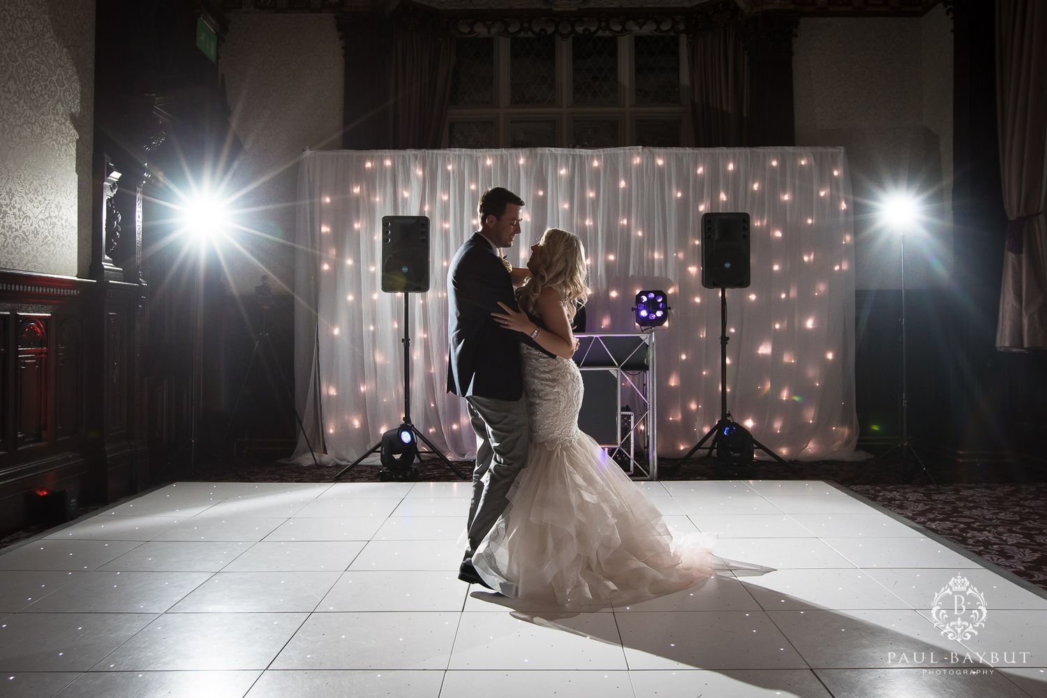 A couple dances in dramatic lighting with a twinkle light backdrop at their wedding reception.