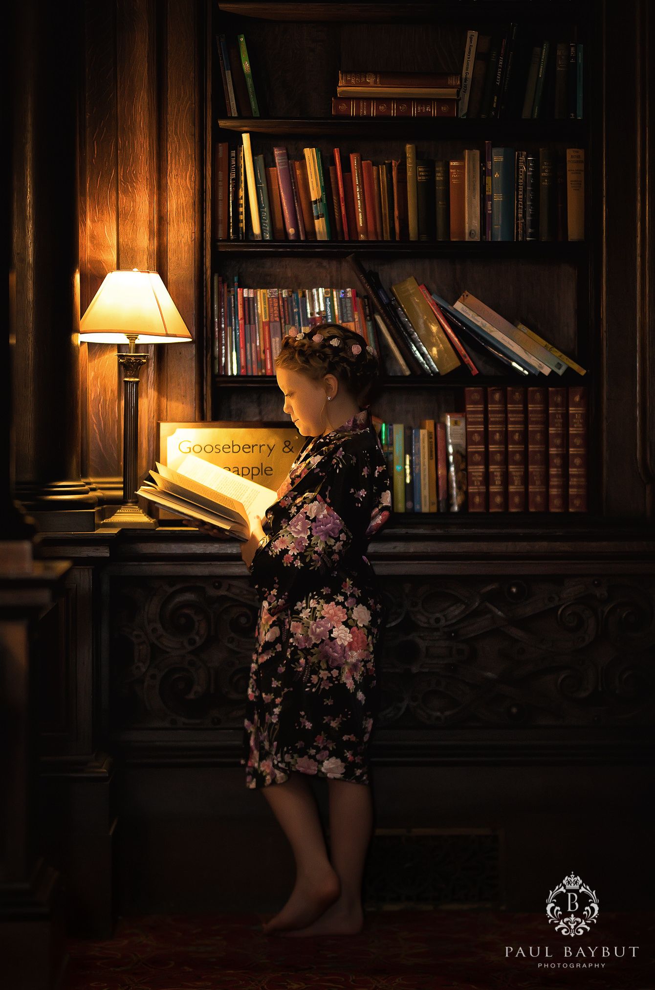 Atmospheric library corner with illuminated desk lamp and floor-to-ceiling bookshelves.