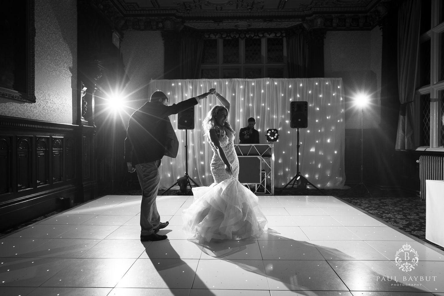 Black and white photo of a couple's first dance silhouetted against a wall of fairy lights.