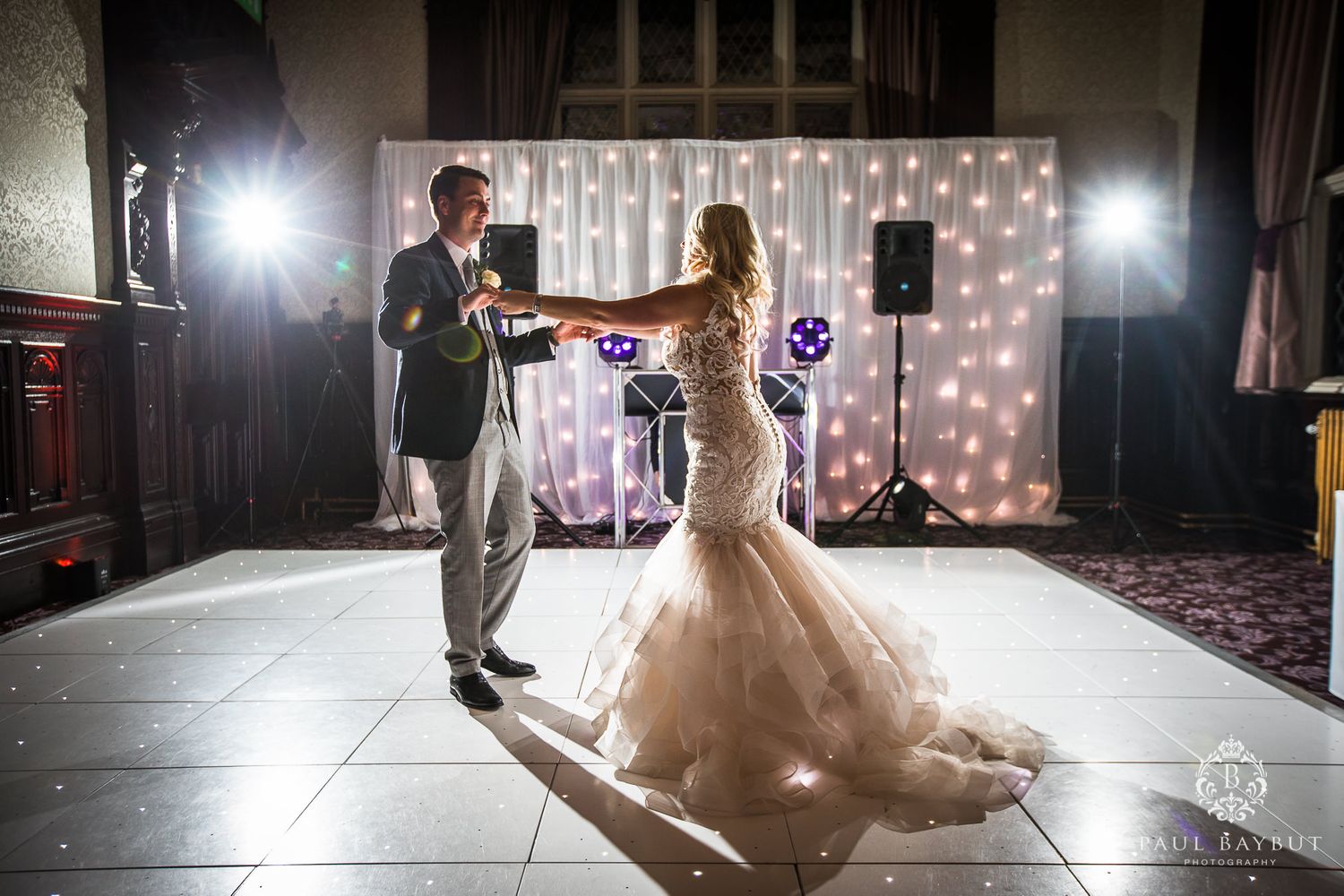 Couple dancing on a spotlit dance floor with twinkling fairy lights and DJ setup in background.