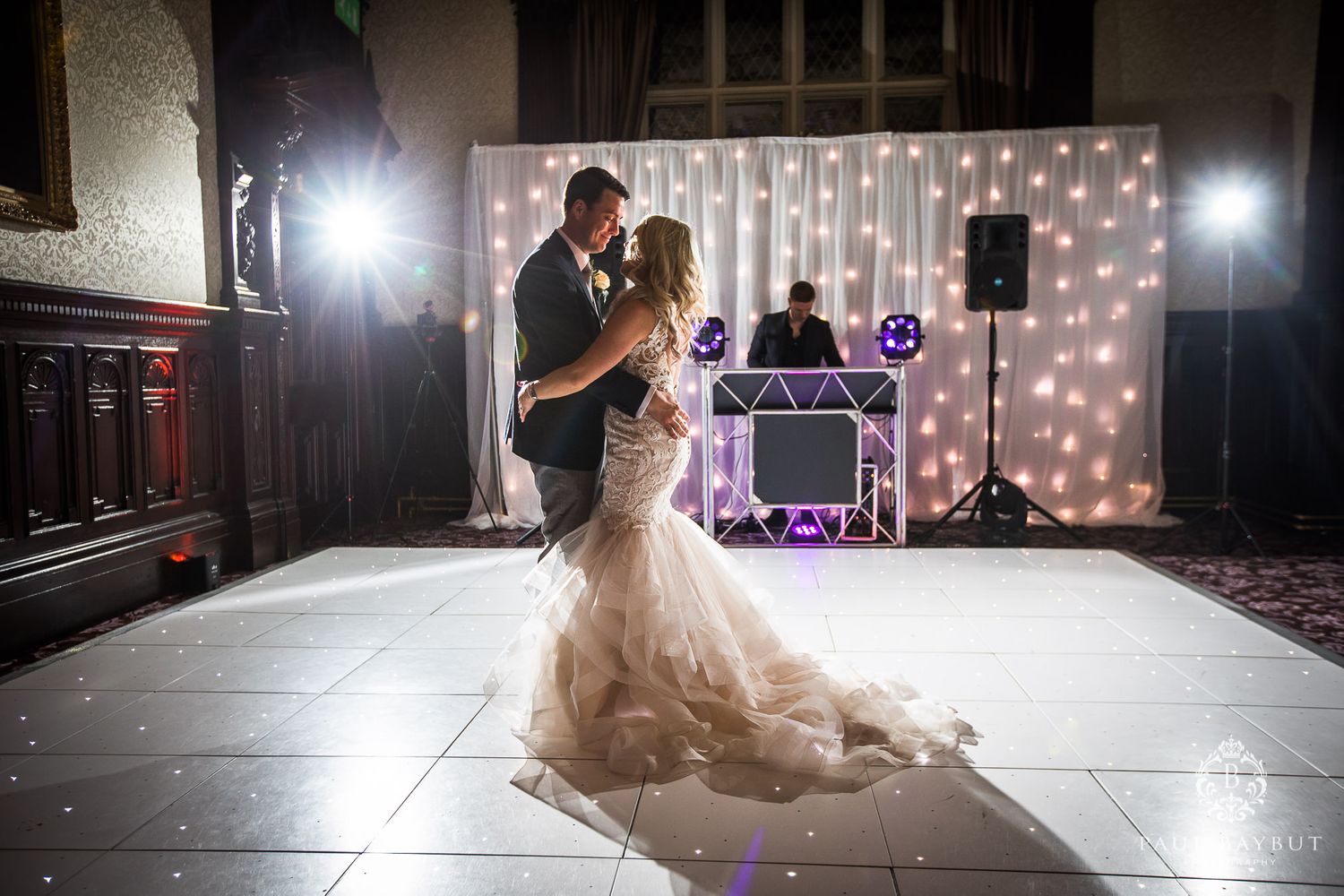 Wedding couple shares an intimate dance moment on illuminated floor with fairy light backdrop.