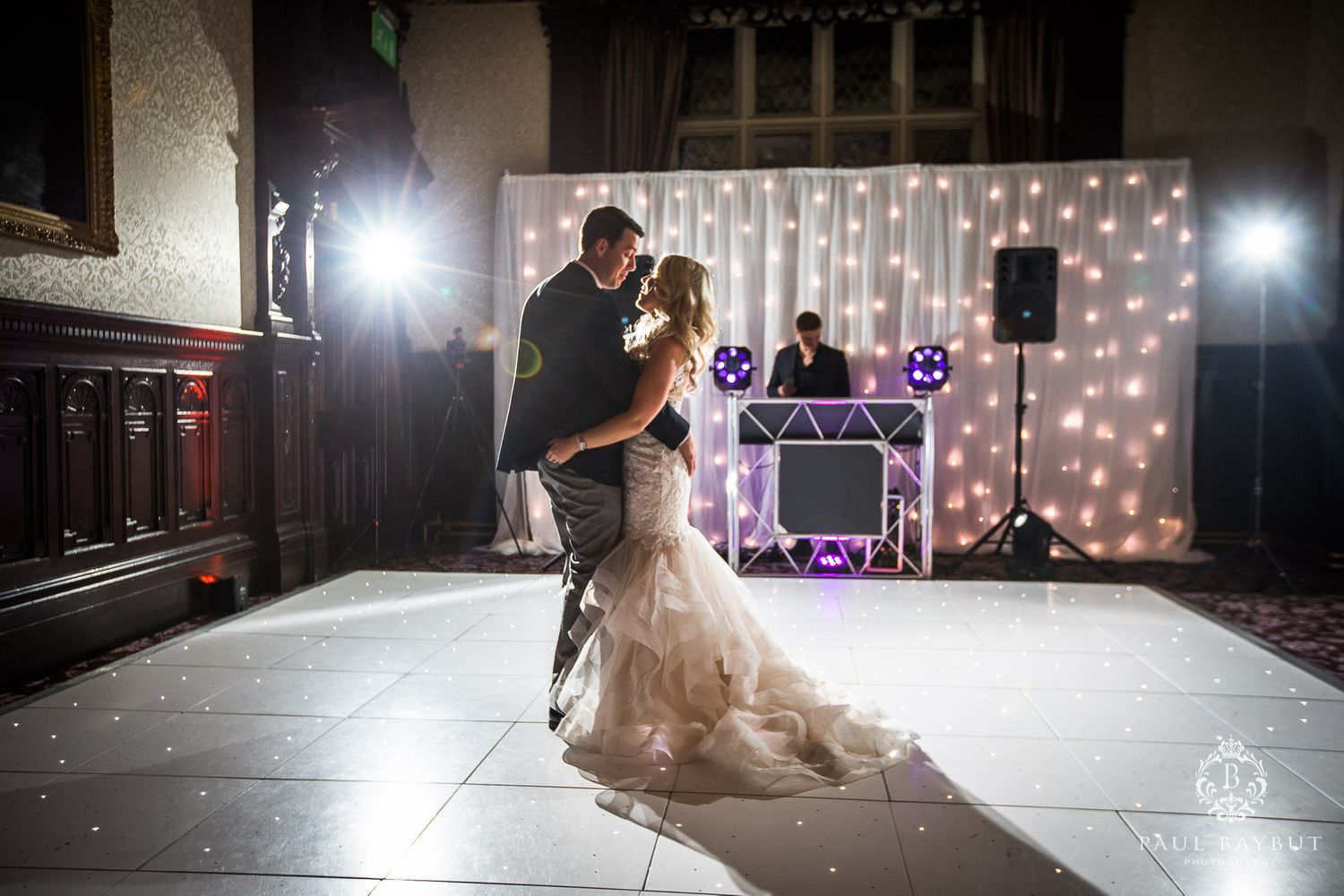 Dramatic dance floor moment captured with spotlights and twinkle light backdrop at wedding reception.