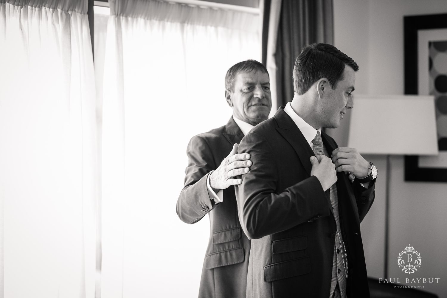 Black and white photo showing two men helping each other prepare formal attire.