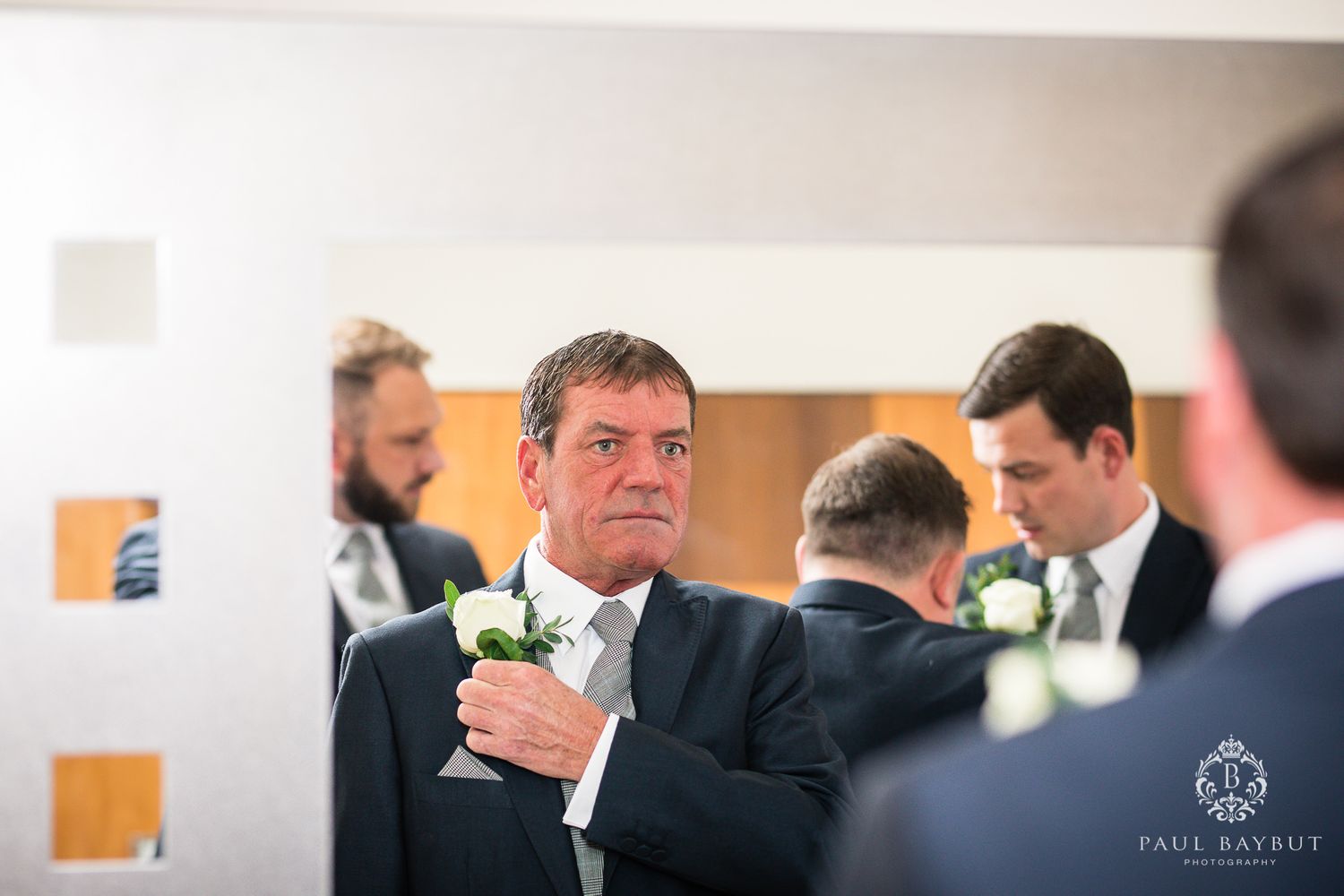 Candid moment captures groomsman adjusting boutonniere during wedding preparations.