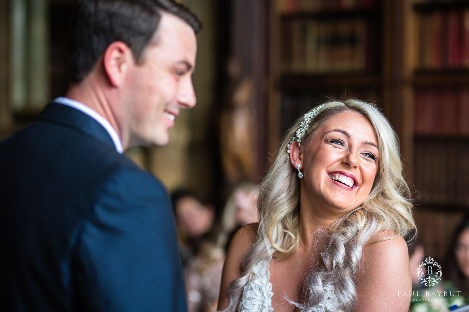 A happy couple shares a laugh during their wedding ceremony in a grand library.