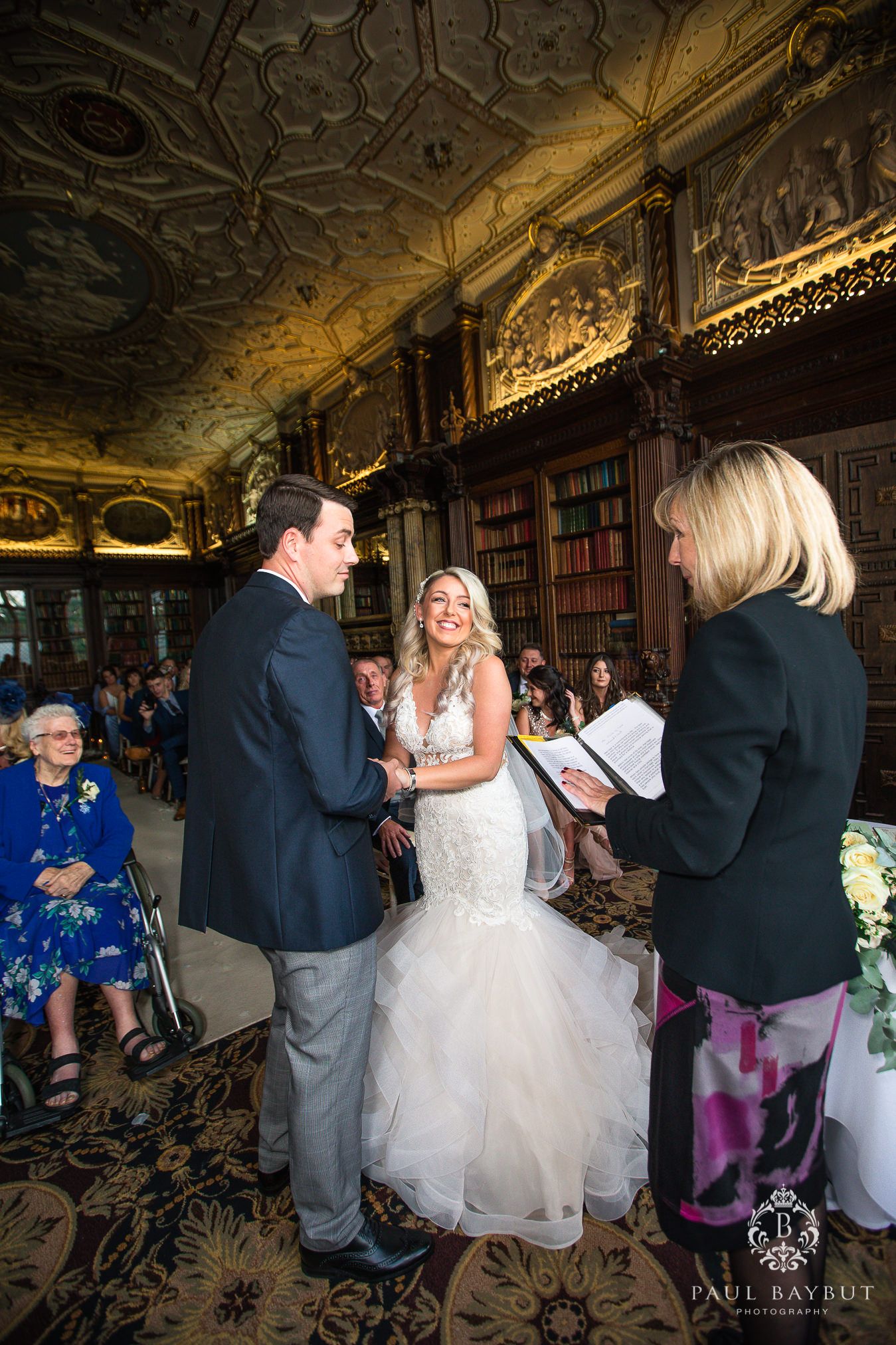 Couple exchanging vows in an elegant library with carved wooden details and decorative ceiling.