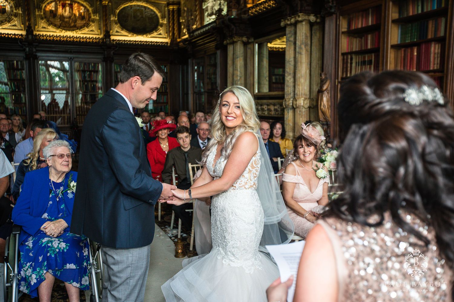 Wedding ceremony in progress inside an elegant library with gilded architectural details.