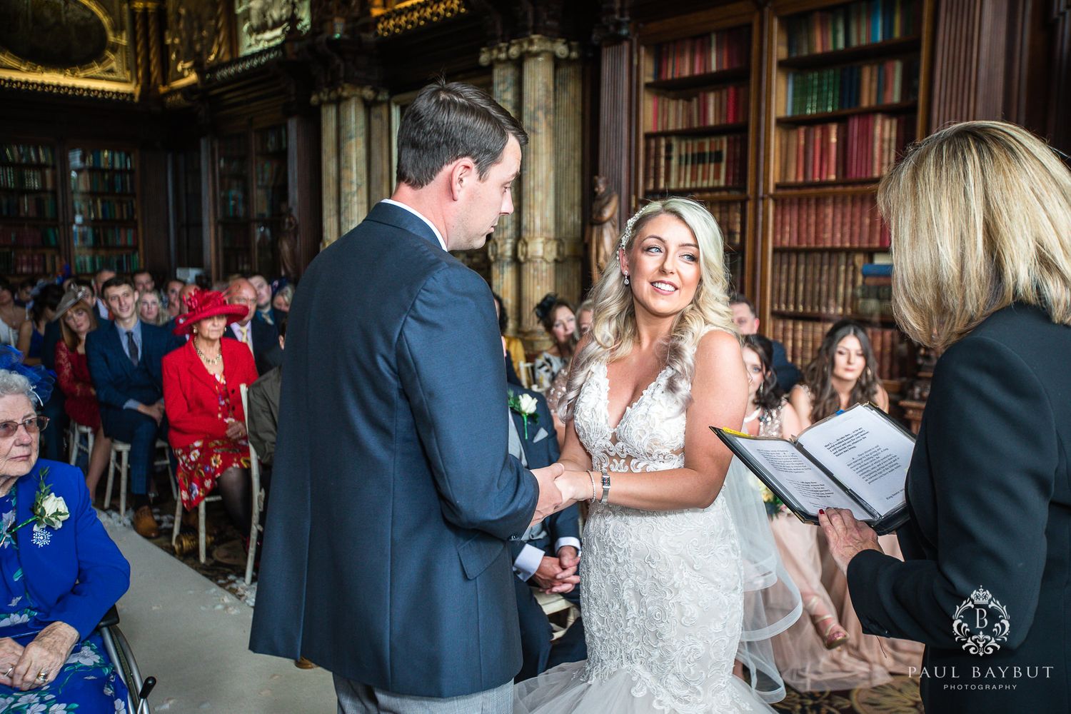 Wedding ceremony in historic library with vintage bookshelves and decorative ceiling.