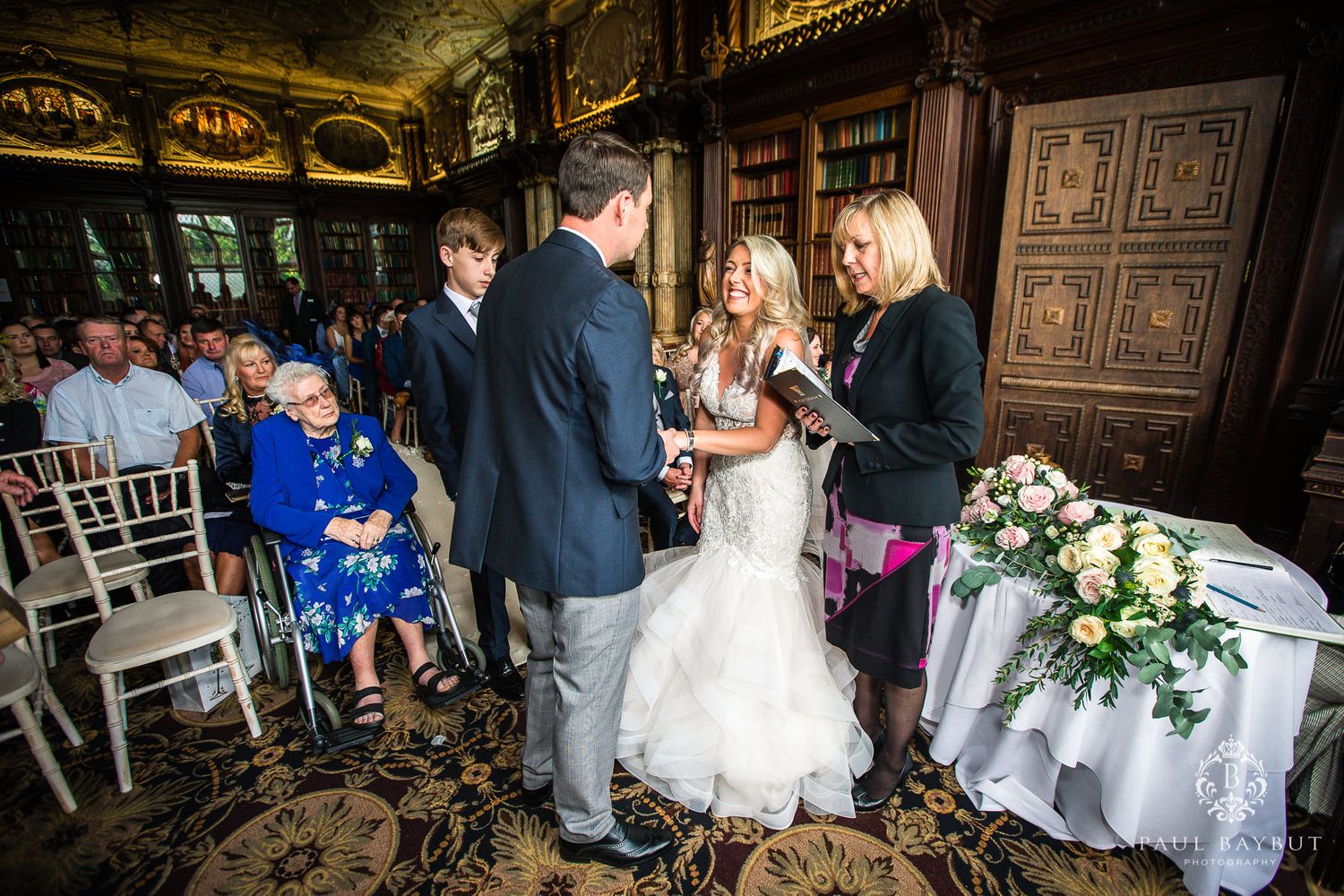 Wedding ceremony in elegant library with guests seated on chiavari chairs.