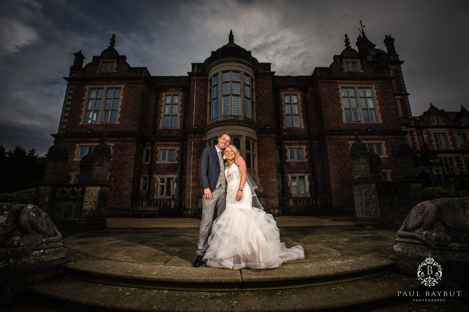 A grand Victorian mansion provides a moody backdrop for a wedding portrait on curved stone steps.