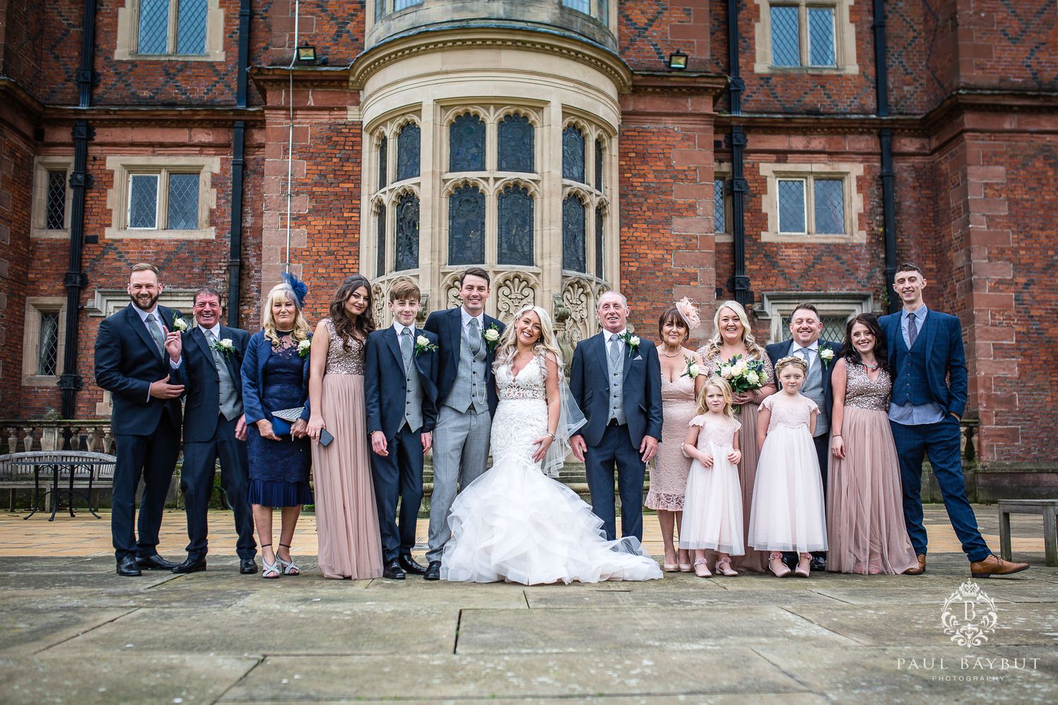 A wedding party poses together on the steps of a historic red brick mansion.