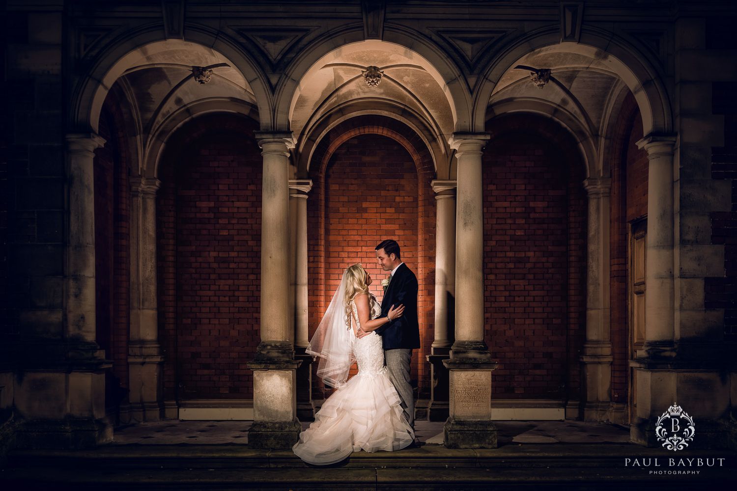 A romantic wedding portrait framed by three arched columns with dramatic lighting.