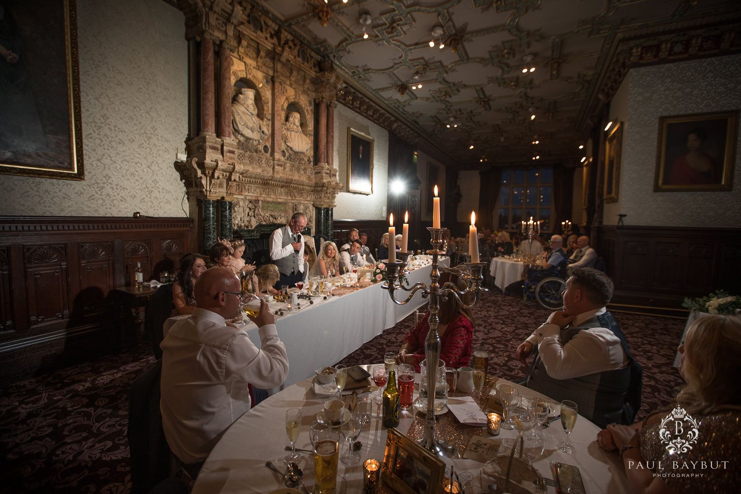 Grand dining hall set for wedding reception with candlelight and historic wooden paneling.