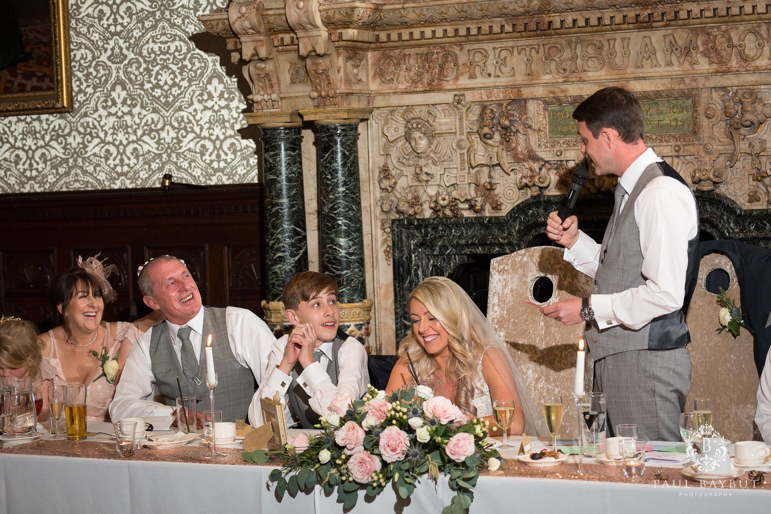 Wedding party listening to speeches during reception at an elegant vintage venue.