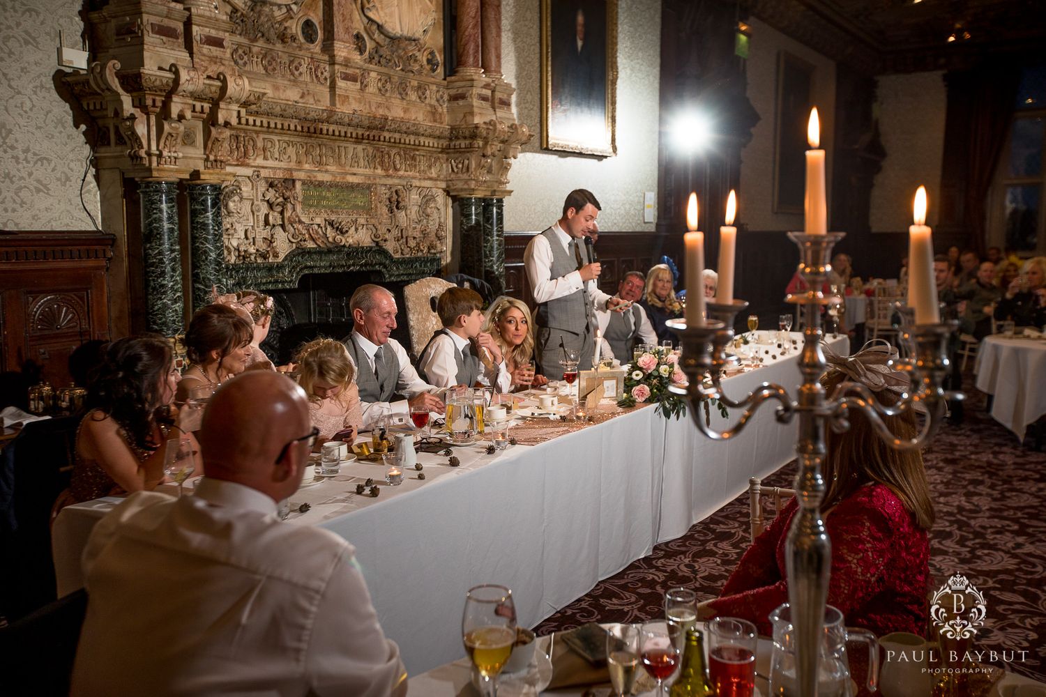 Elegant wedding reception dinner table with lit candles in an ornate room with wood paneling and carved details.
