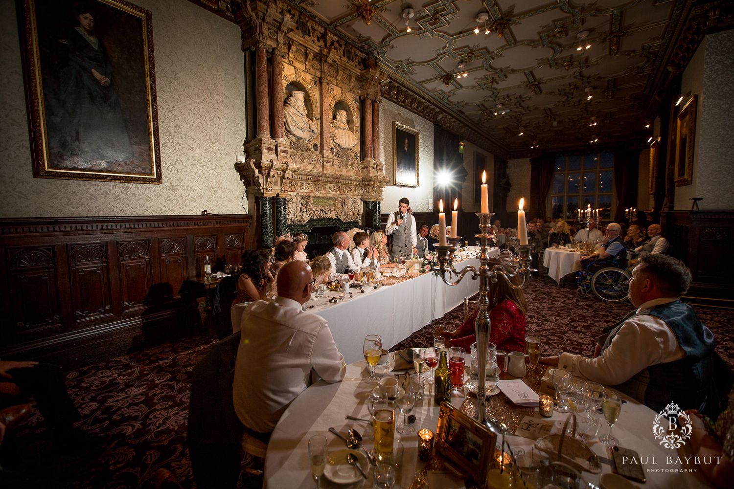 Romantic candlelit wedding reception dinner in a grand historic hall with ornate woodwork and decor.