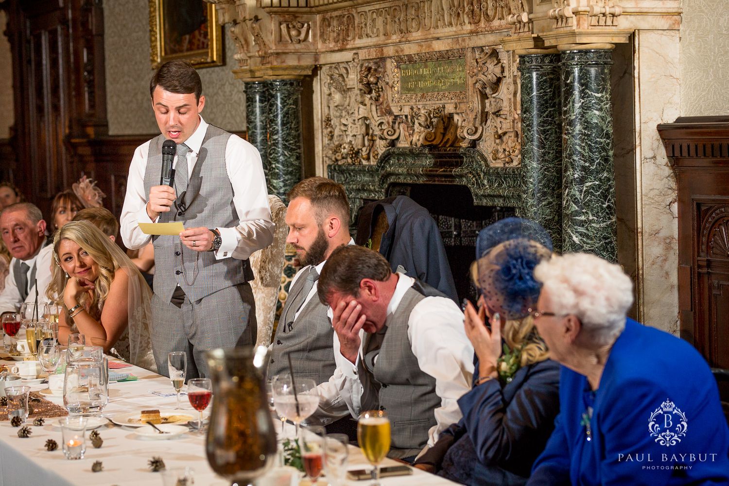 Wedding reception speech at a long banquet table in a historic manor room with candlelight.