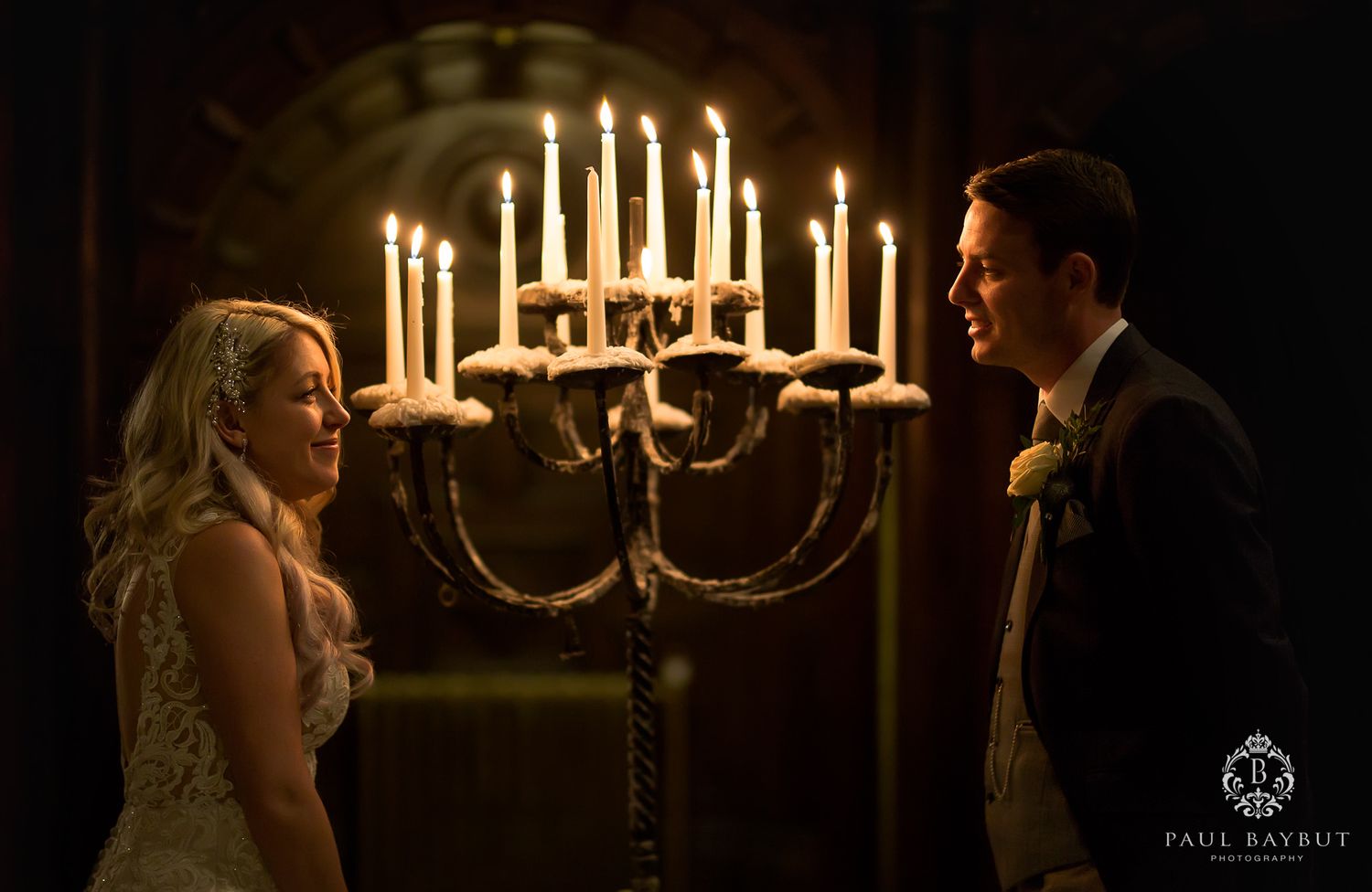 Romantic couple illuminated by candlelight beneath an elegant chandelier in a historic venue.