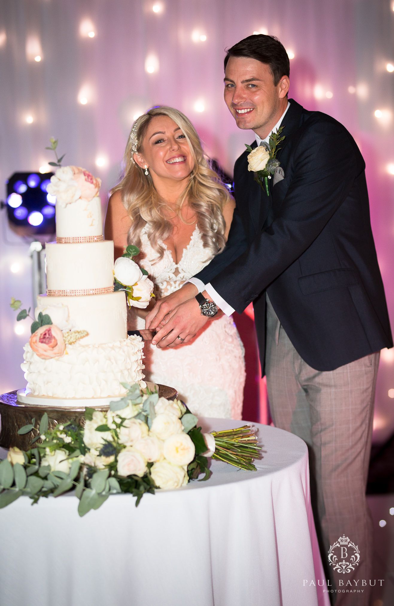 A wedding couple cuts their elegant white tiered cake decorated with flowers at their reception.