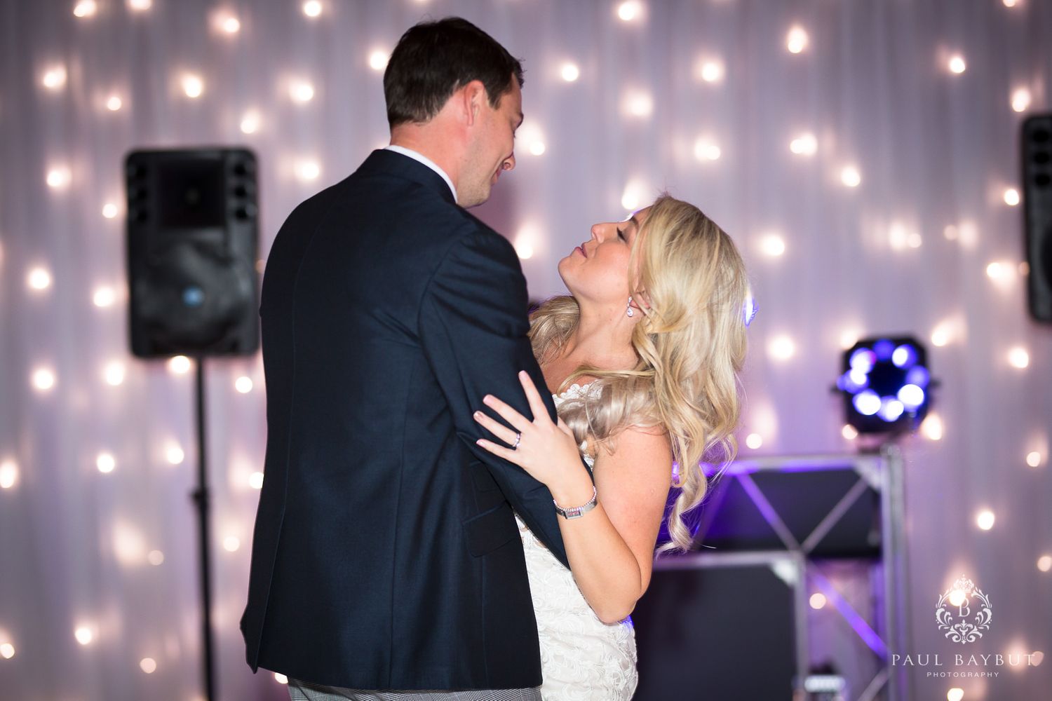 Couple shares a romantic moment during their first dance with string lights creating a magical backdrop.