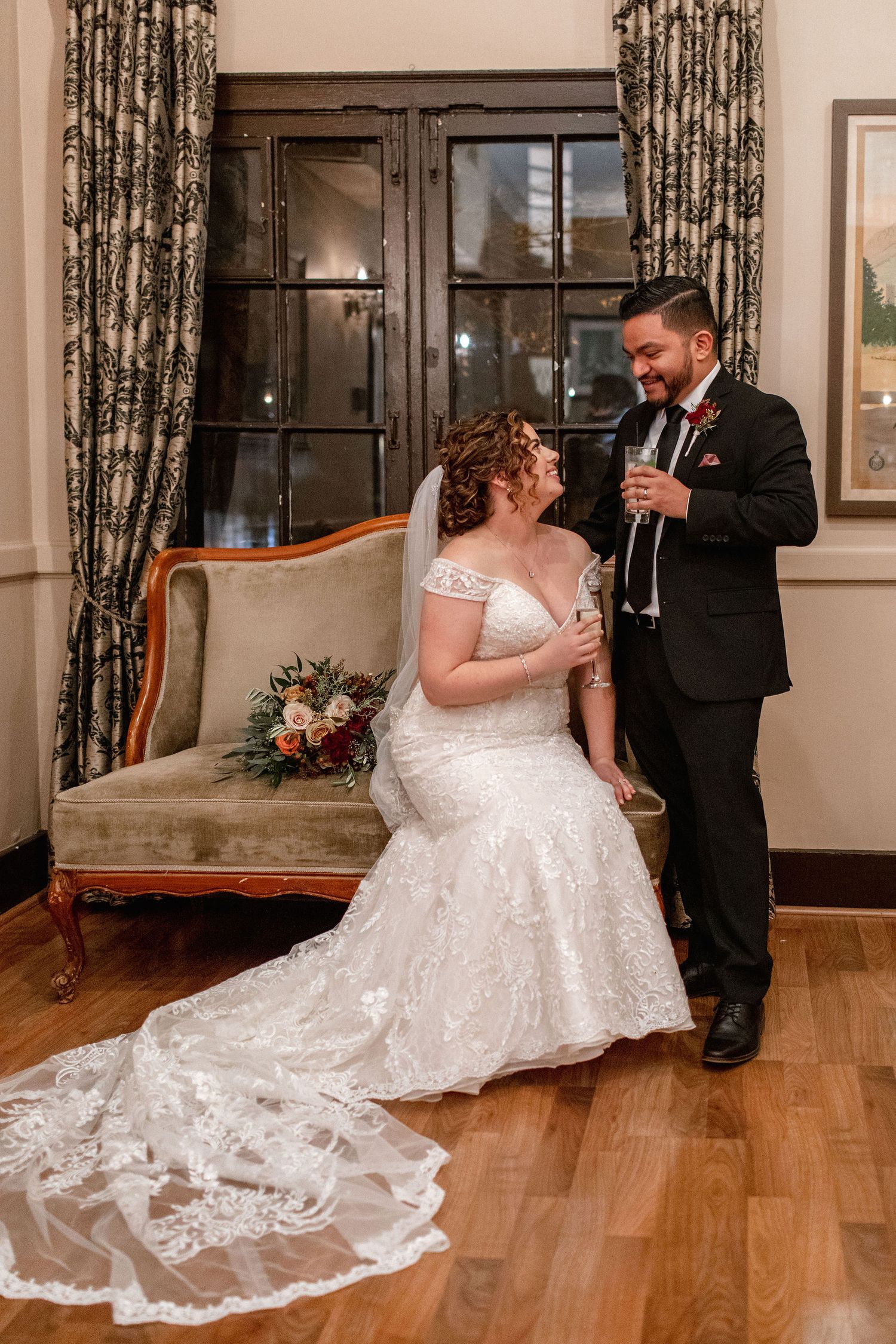 A couple sharing a joyful moment in an elegant room with vintage furniture and floral curtains.