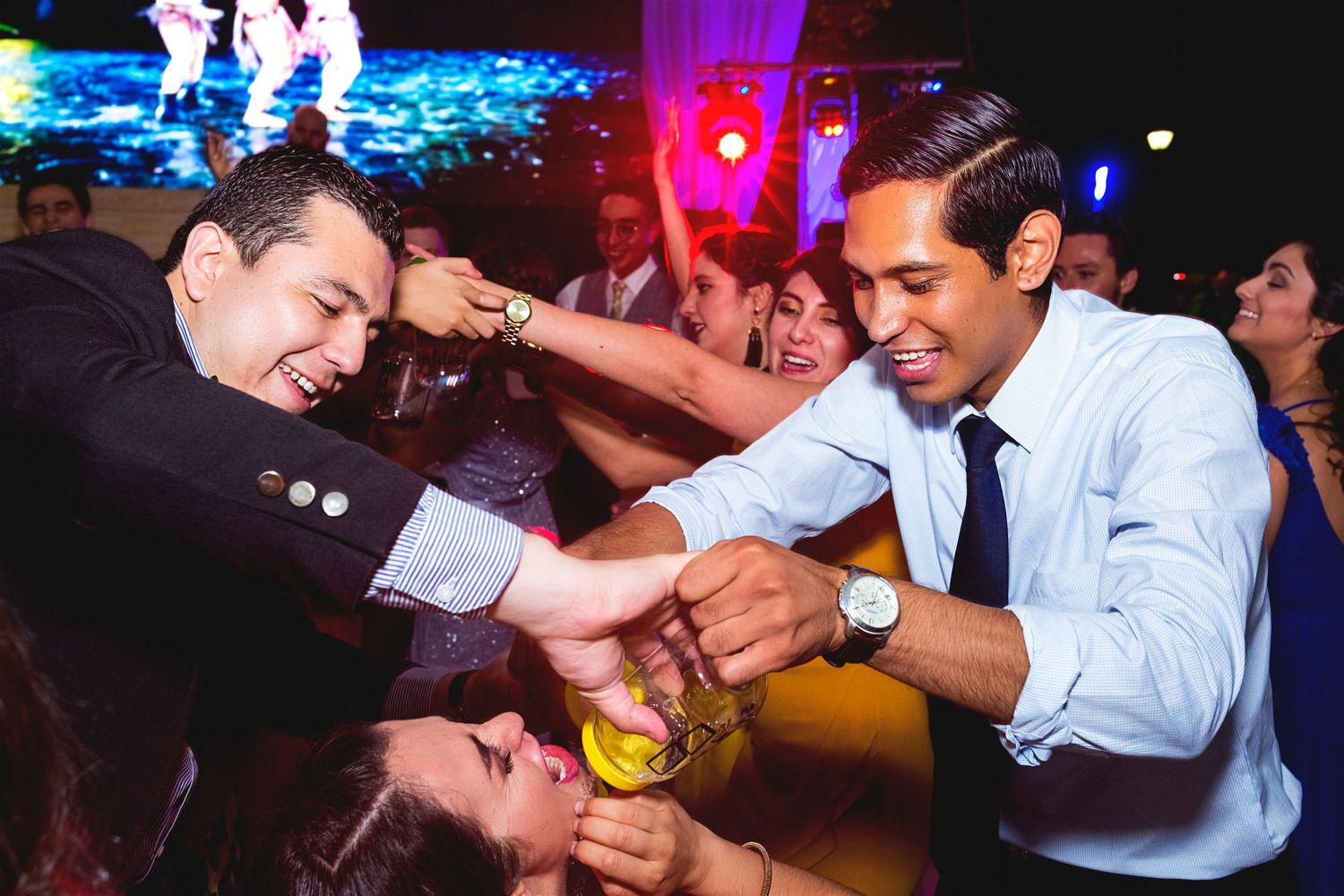 Two guests playfully struggle over a bottle on a colorful dance floor at a reception party.