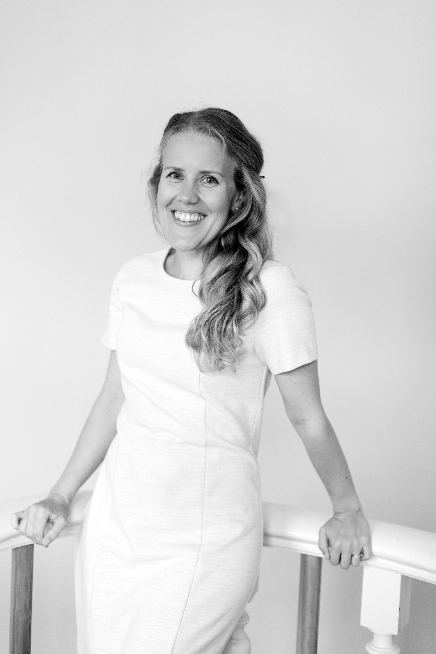 Black and white portrait of photographer in white dress leaning on railing.