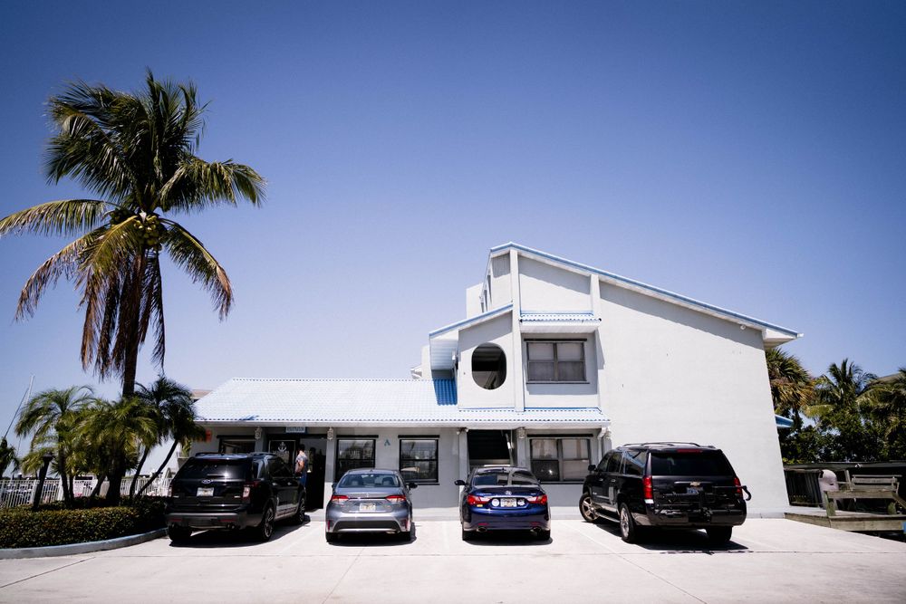 White modern beach house with palm trees and parked cars in tropical setting.