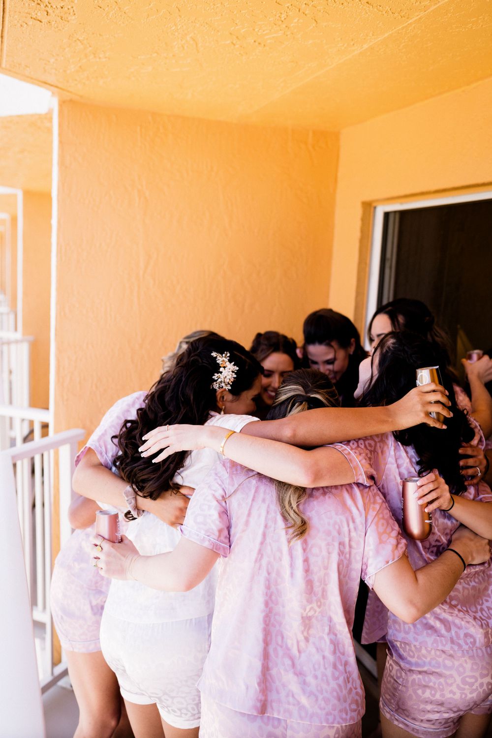 Group huddle of friends in pink and white outfits sharing a joyful moment on a balcony.