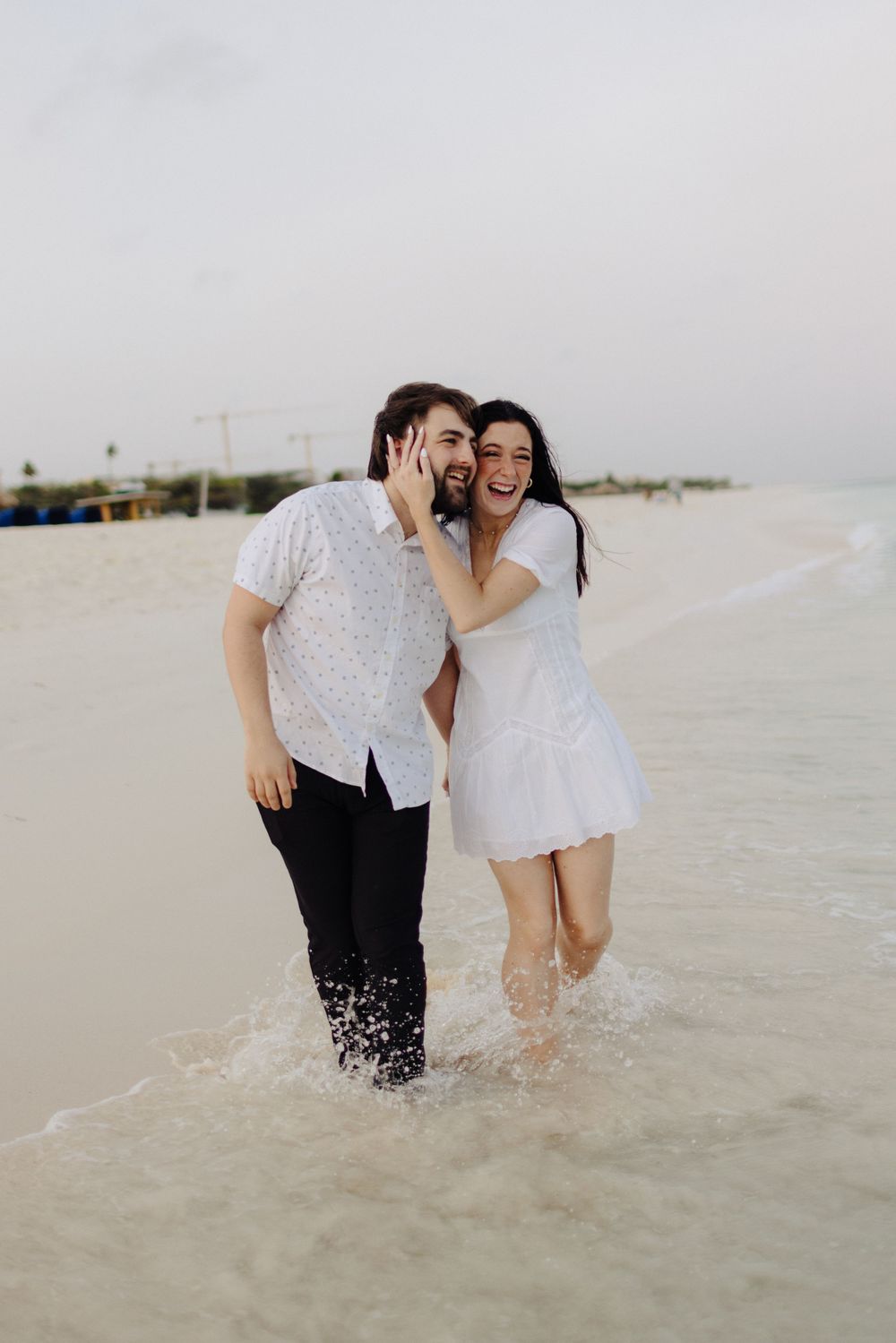 Joyful couple laughing together while standing in shallow ocean water at the beach.