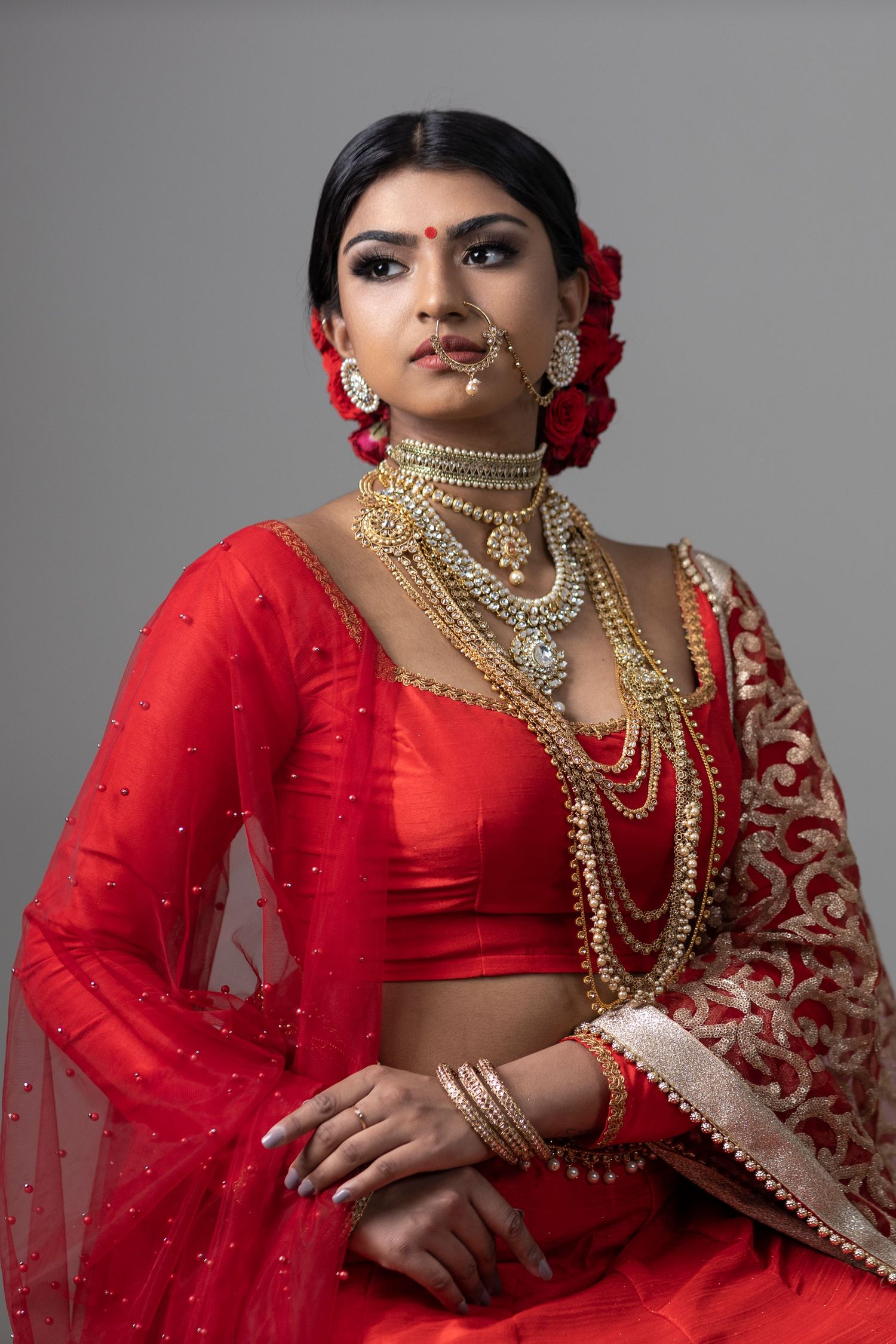 Traditional South Asian bridal look featuring red lehenga with intricate gold jewelry and flowers.
