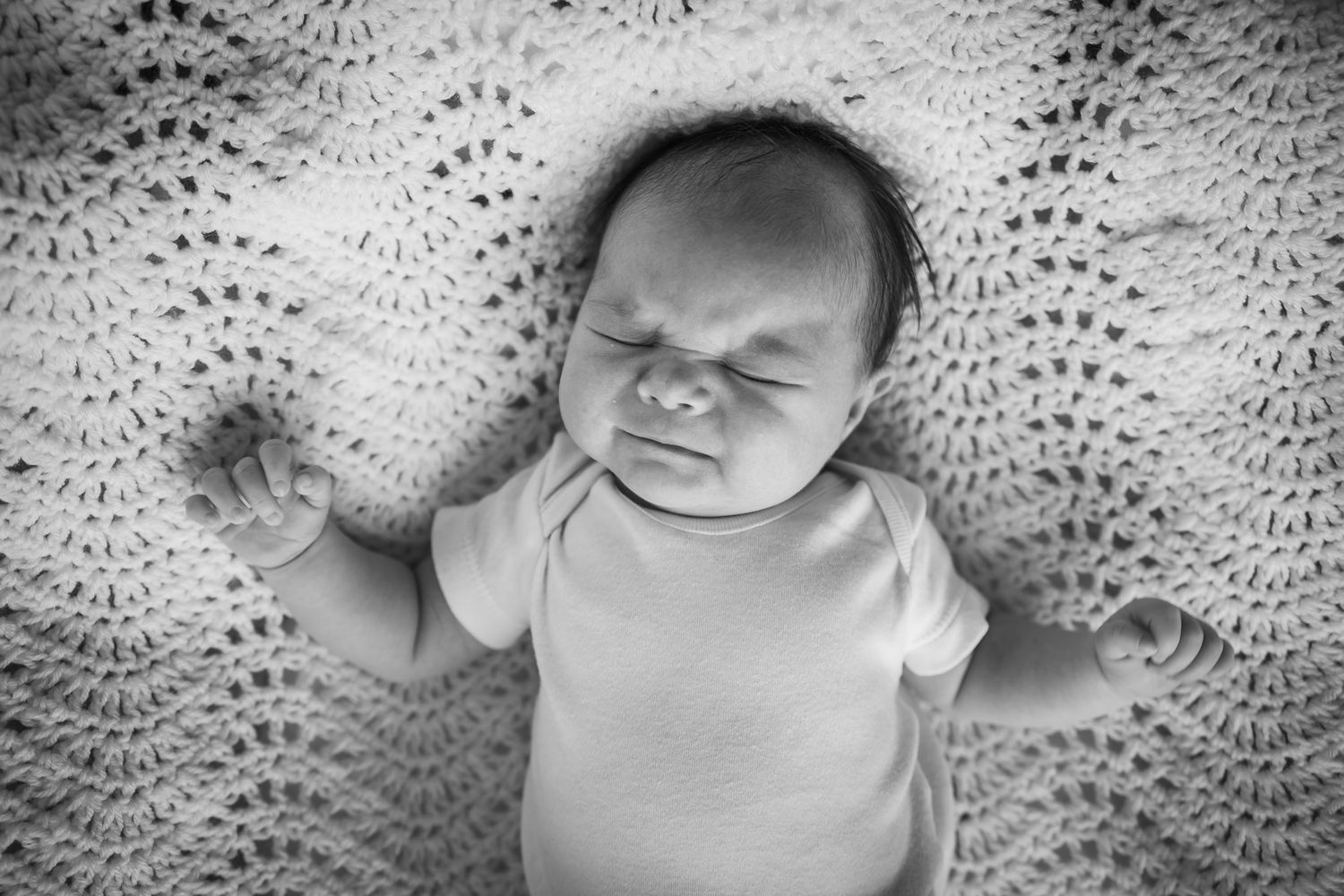 Baby sleeping on textured blanket in black and white photography.