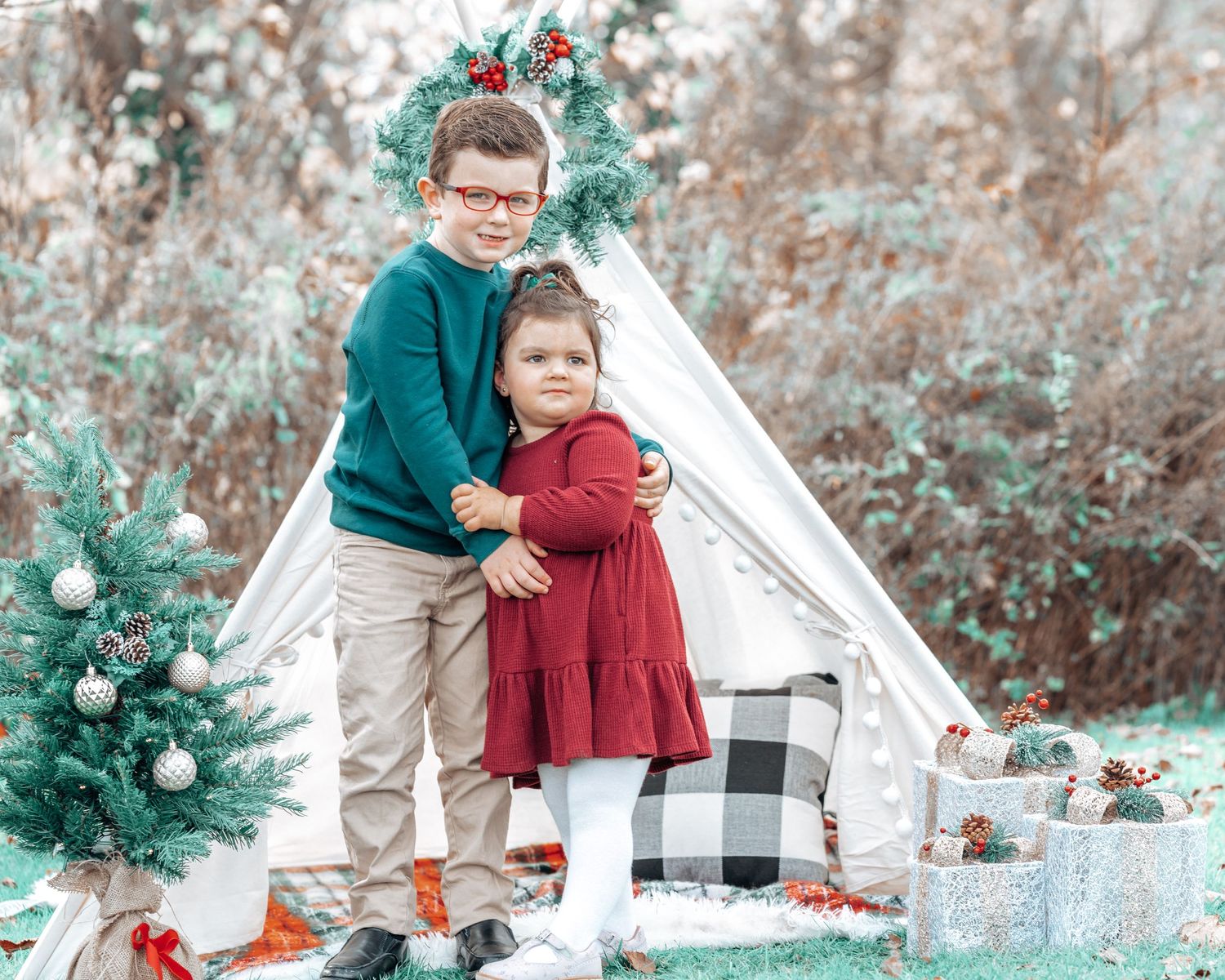 Children pose in front of a white teepee tent with Christmas decorations and buffalo plaid pillows.