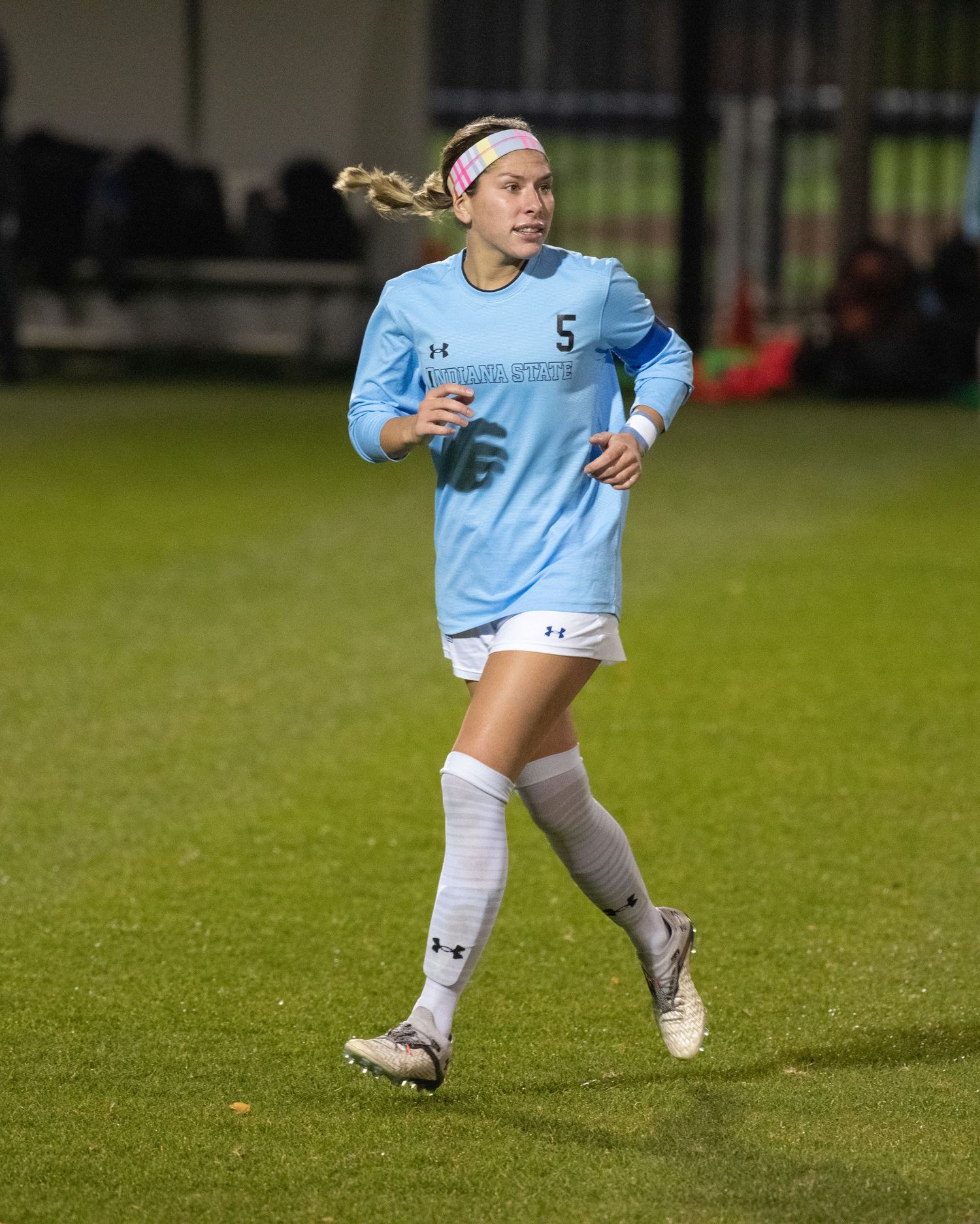 Soccer players in light blue uniforms running on grass field during nighttime match.