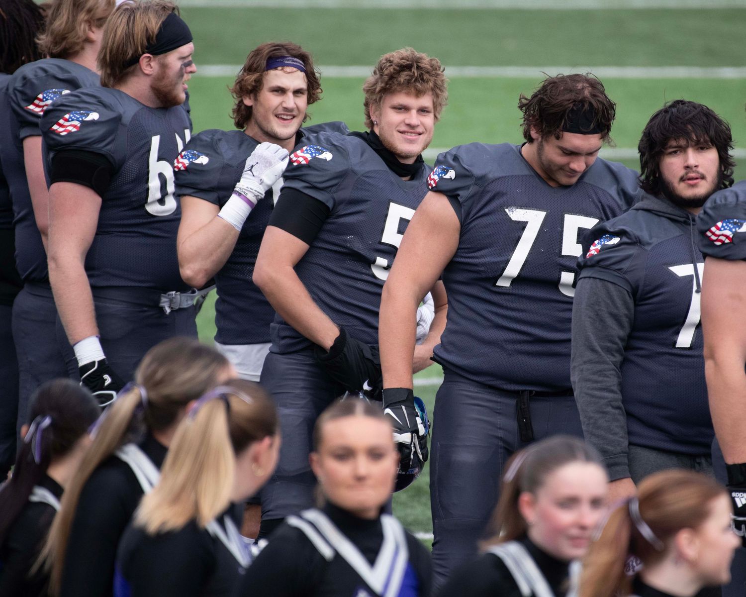 Football players in black uniforms gathered on the sidelines during a game.