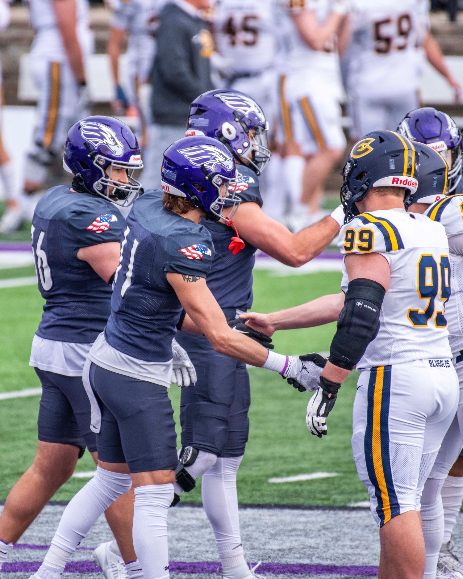 Football players from opposing teams shake hands on the field after a game.