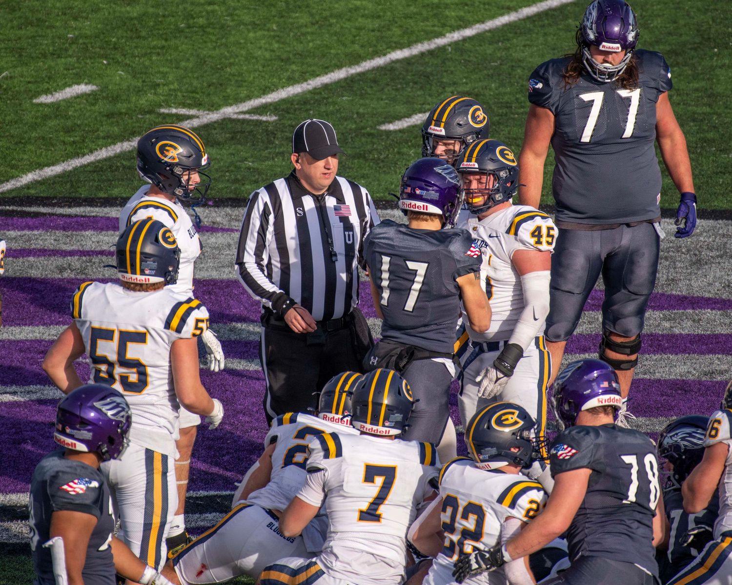 Football players and officials gather on field during game discussion.