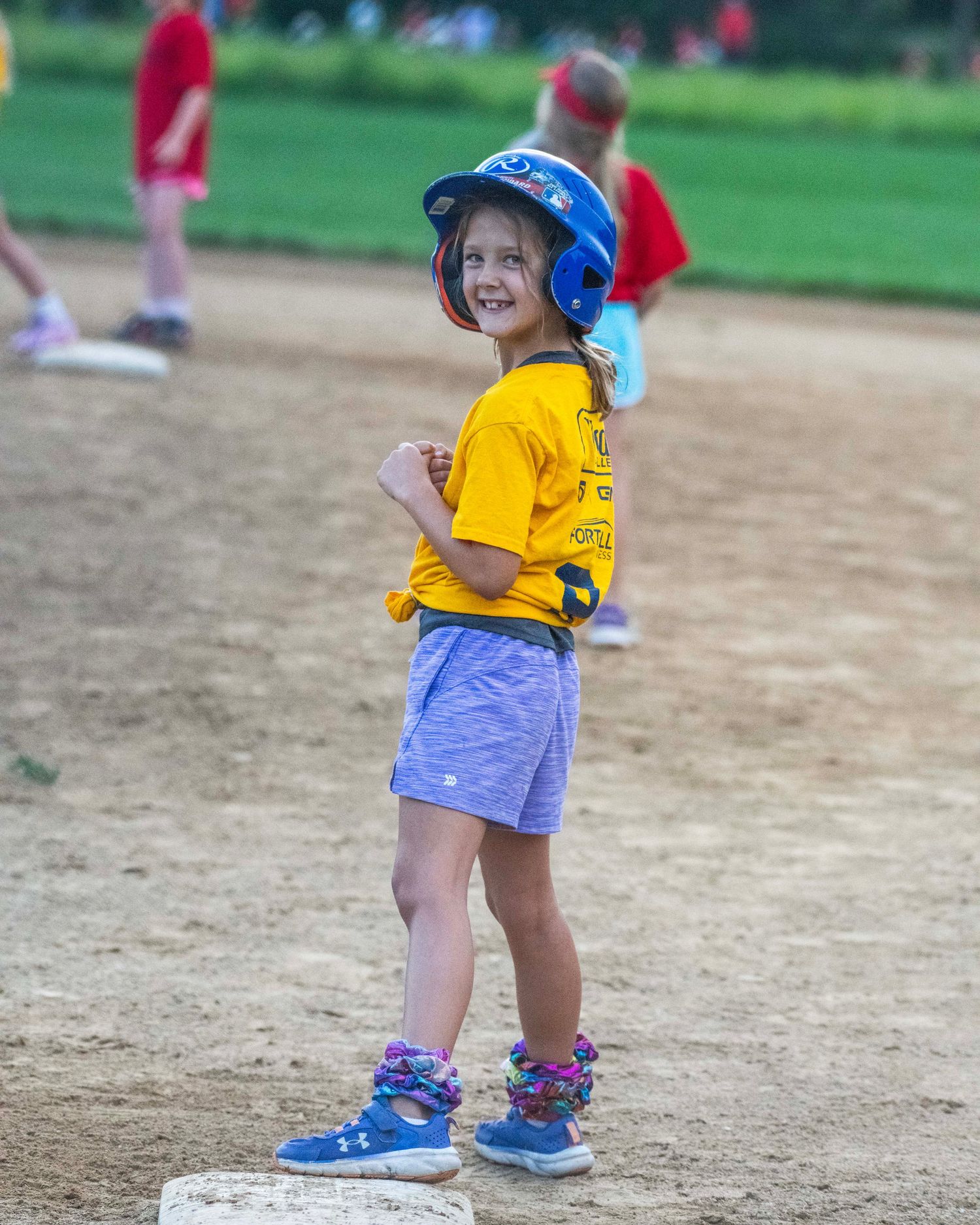 Toddler wearing a sun hat playing baseball on a dirt field.