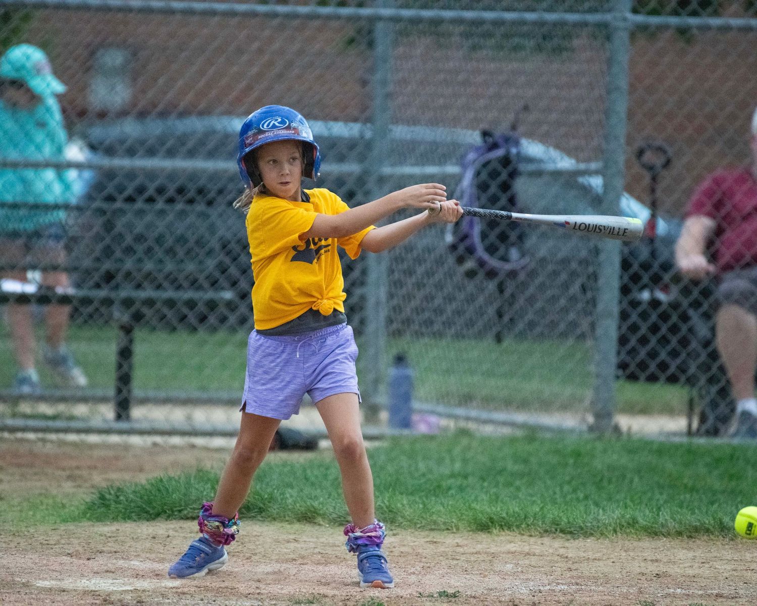Young child in blue shoes playing t-ball on a baseball diamond.