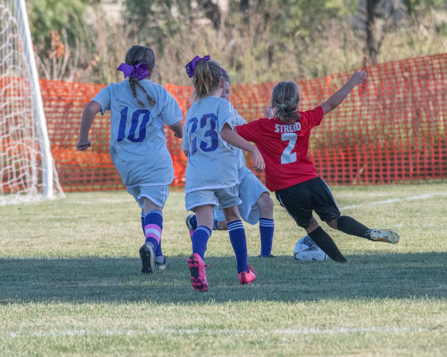 Soccer players dive to block goal during intense youth match.