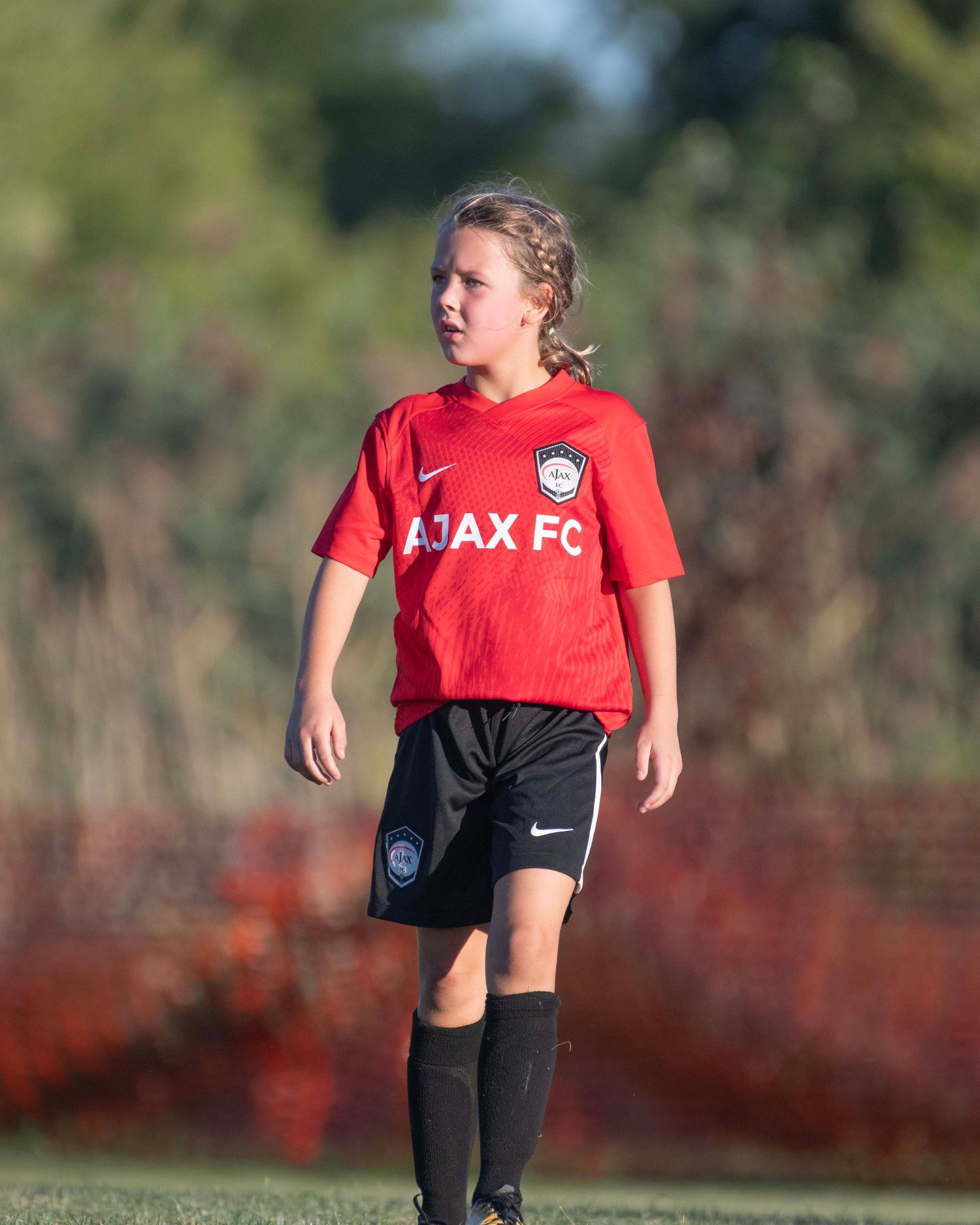 Soccer player in red jersey and black shorts dribbling on a grass field during training.