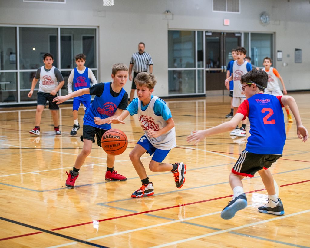 Youth basketball players running drills on a wooden court in blue jerseys.